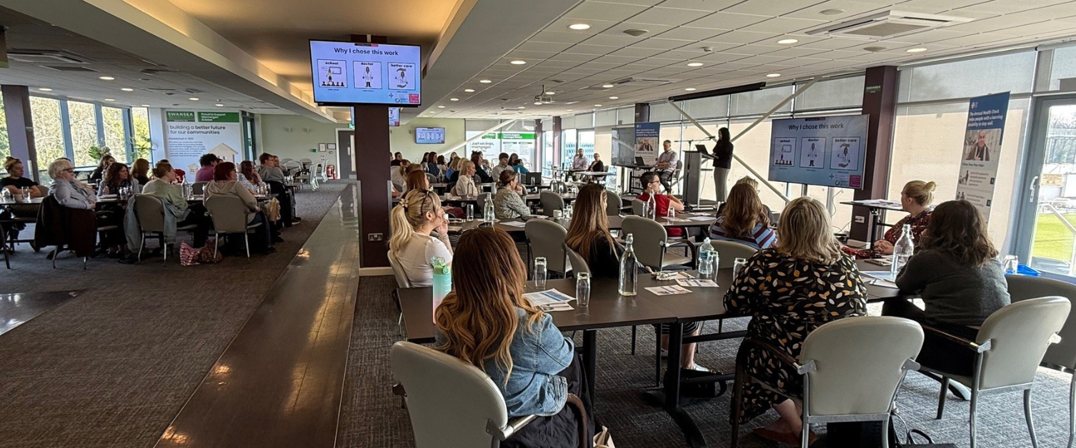 A large group of people are watching a presentation in a conference room.