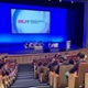 A lecture theatre is full of people watching five people on stage give a talk.