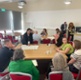 <span style="background-color: rgb(234, 244, 253);">People are sat around a table having a conversation and writing on flip chart paper as part of a workshop session taking place at conference</span>