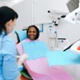 A dentist talks to a smiling person sat on a dentist’s chair who is waiting for treatment.