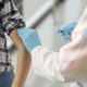 A healthcare professional gives a vaccination to a person with their sleeve rolled up.