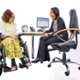 A person in a wheelchair speaks to a healthcare professional sat at a desk.