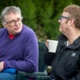 Two men are drinking water and tea as they sit and chat on a bench in the park.