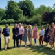 Two teams of people are stood side by side on a green garden surrounded by trees.